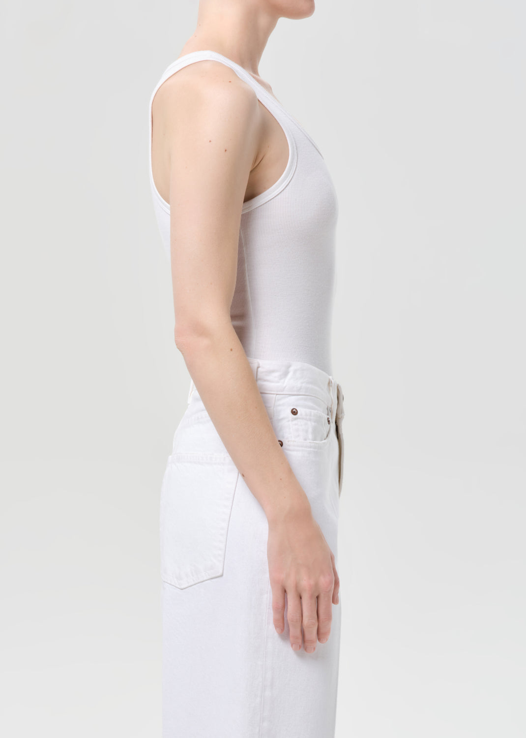 Person wearing a white tank top and pants on a plain background