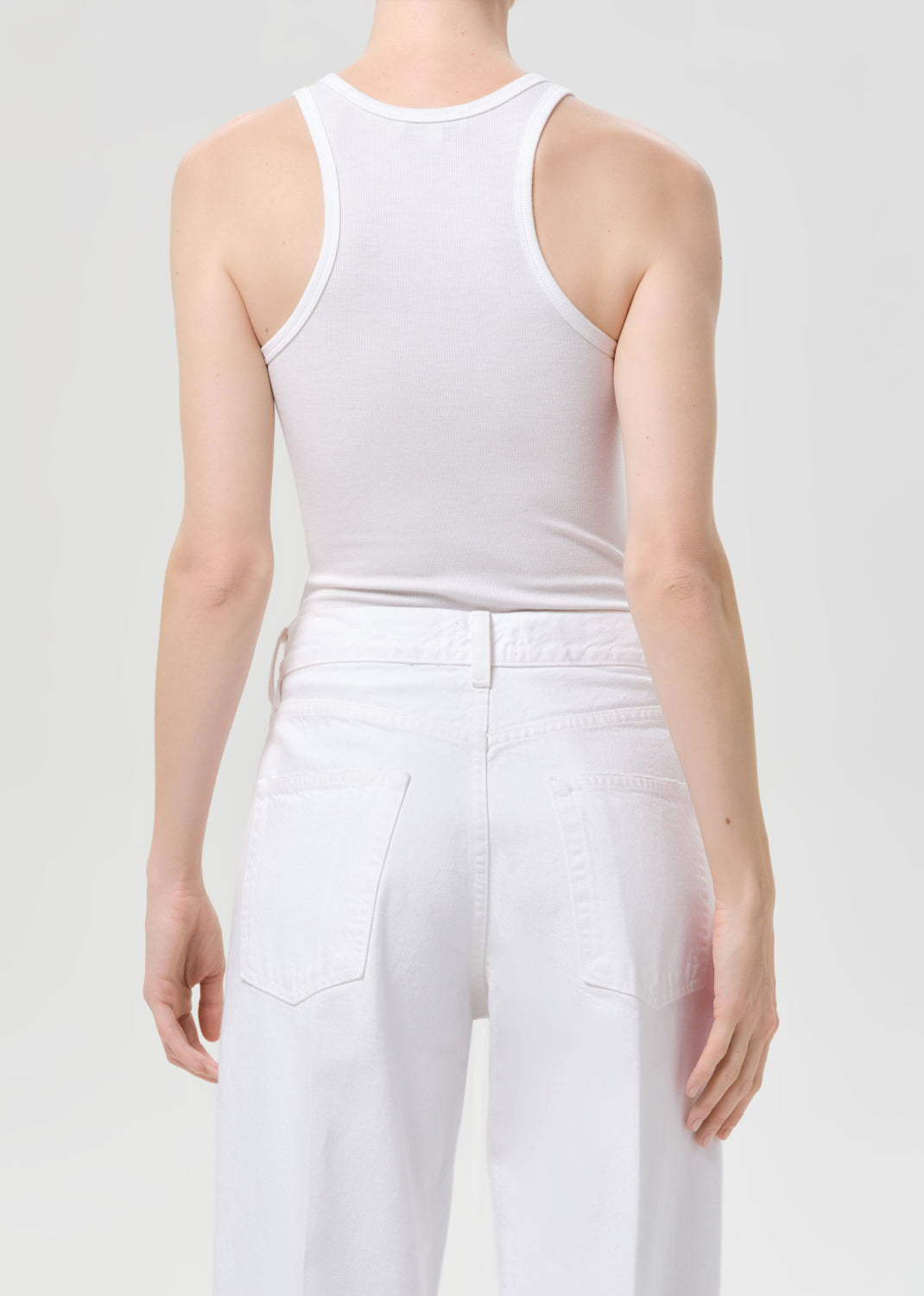 Person wearing a white tank top and pants on a light gray background