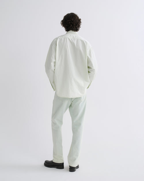 A man viewed from behind wearing a light sage green button-down shirt and matching light sage green trousers, paired with black shoes, against a plain white studio background.