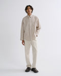 A man modeling a light beige long-sleeve linen button-up shirt and off-white trousers, paired with black loafers, against a plain light gray studio background.