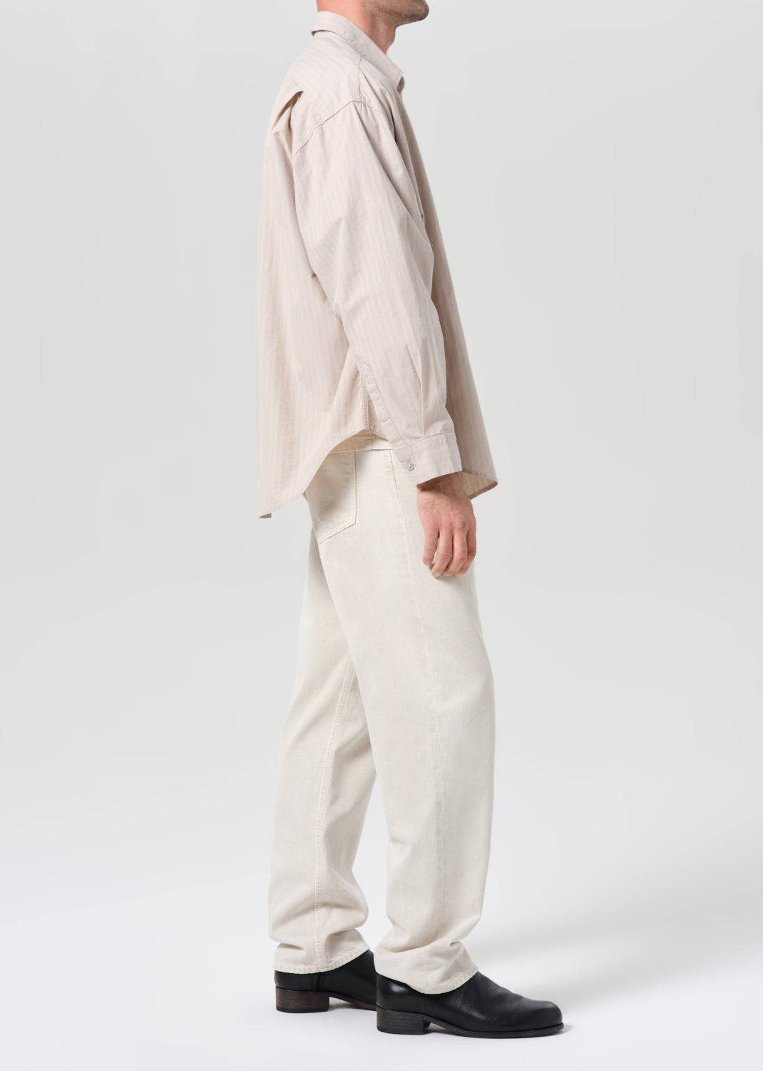 Person wearing a beige shirt and pants with black shoes on a white background