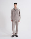 A model stands against a light gray studio background wearing a light gray corduroy button-up shirt jacket with chest pockets, matching light gray corduroy trousers, a white undershirt, and black leather shoes.