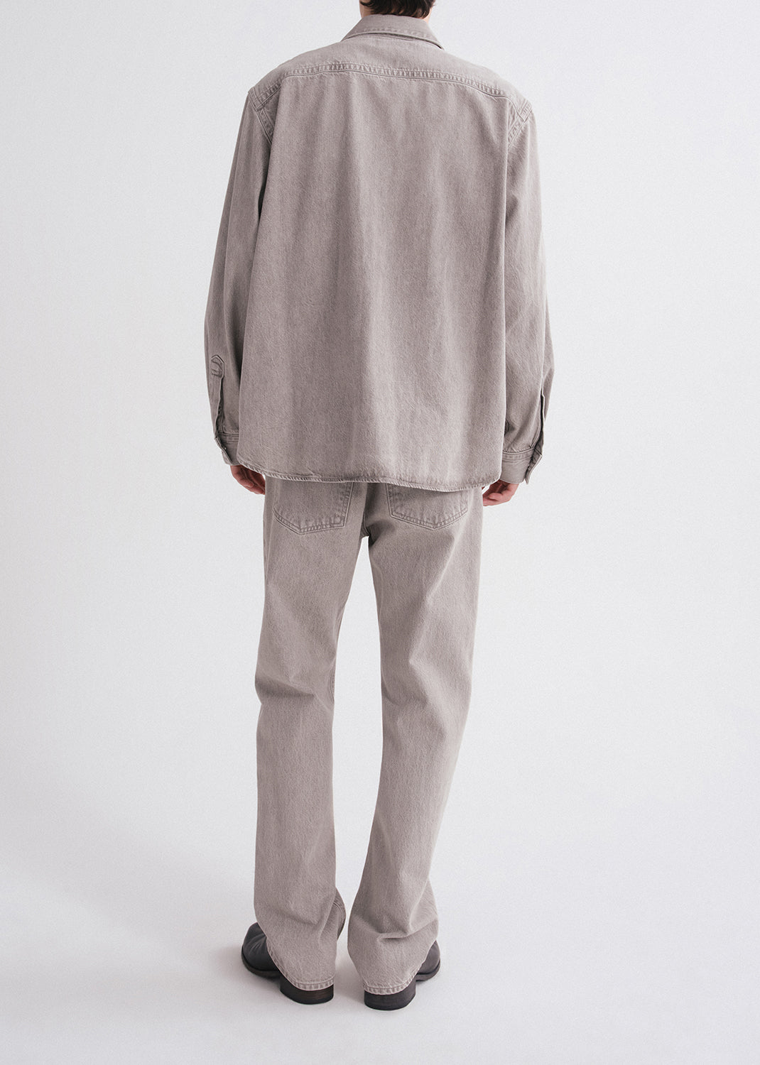 Person wearing a light gray shirt and pants on a grey background