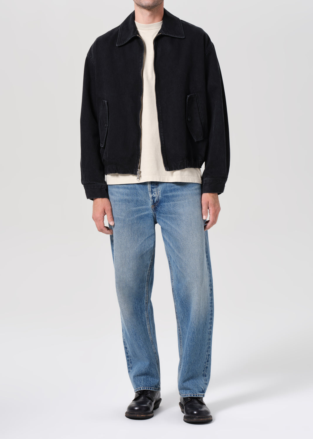 Person wearing a black jacket, white shirt, blue jeans, and black shoes on a white background