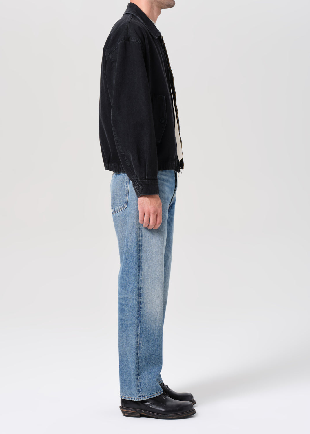 Person wearing a black jacket and light blue jeans on a white background