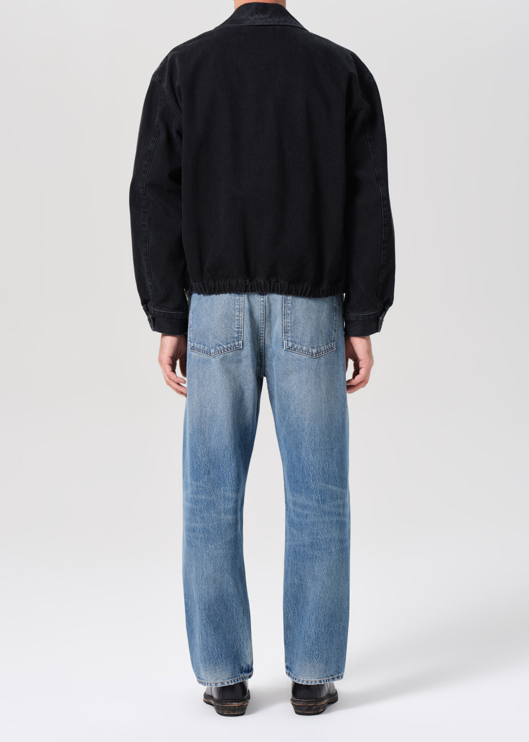 Person wearing a black jacket and light blue jeans on a white background