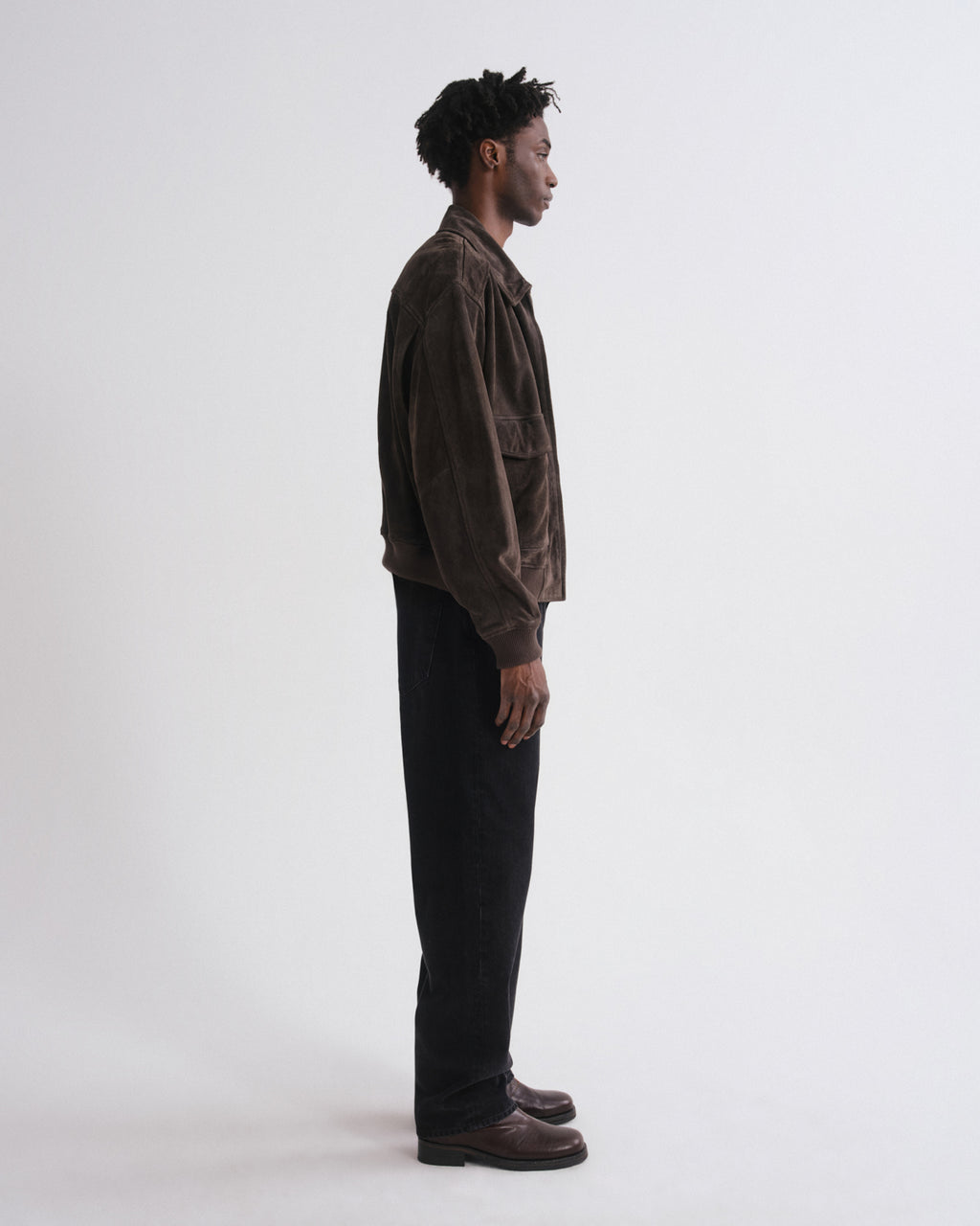 Man wearing a brown jacket and black pants standing against a white background