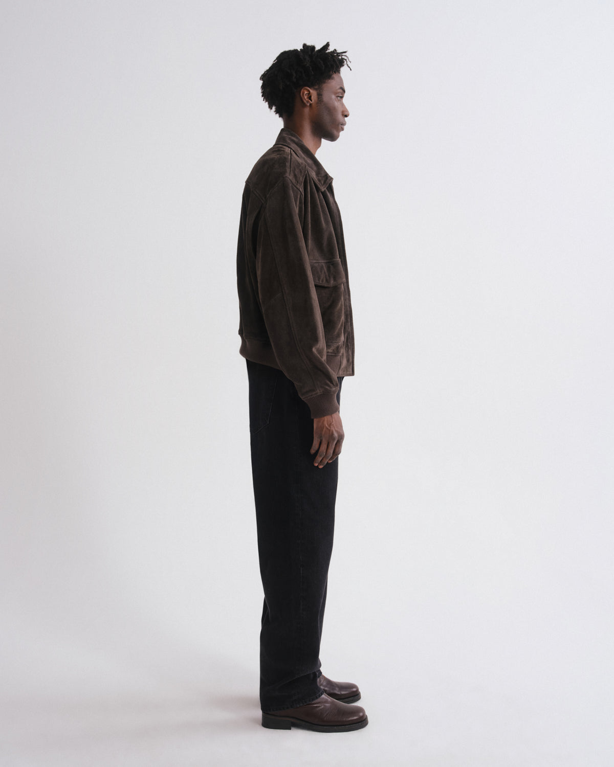 Man wearing a brown jacket and black pants standing against a white background