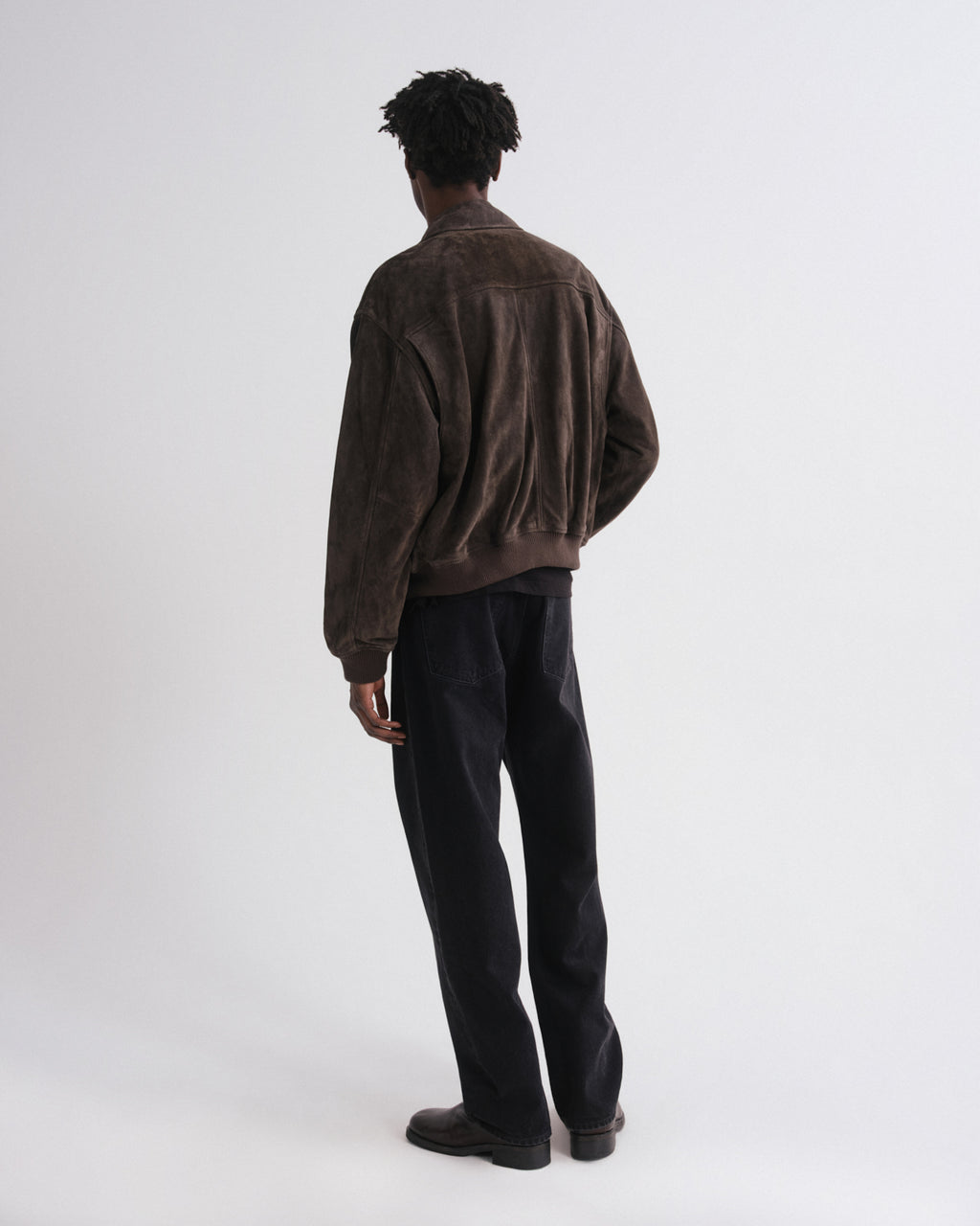 Person wearing a brown jacket and black pants on a white background