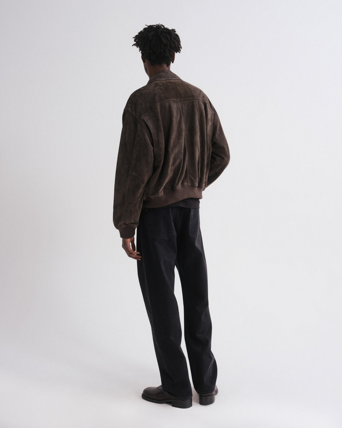 Person wearing a brown jacket and black pants on a white background
