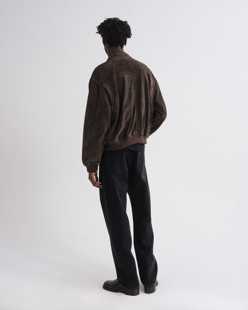 Person wearing a brown jacket and black pants on a white background