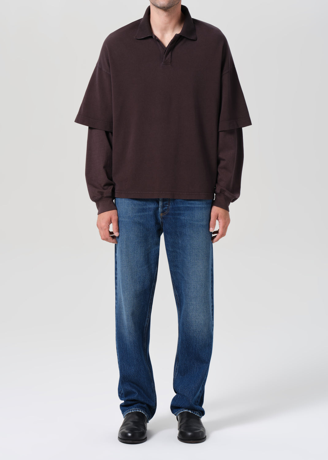 Person wearing a brown long-sleeve shirt and blue jeans on a white background