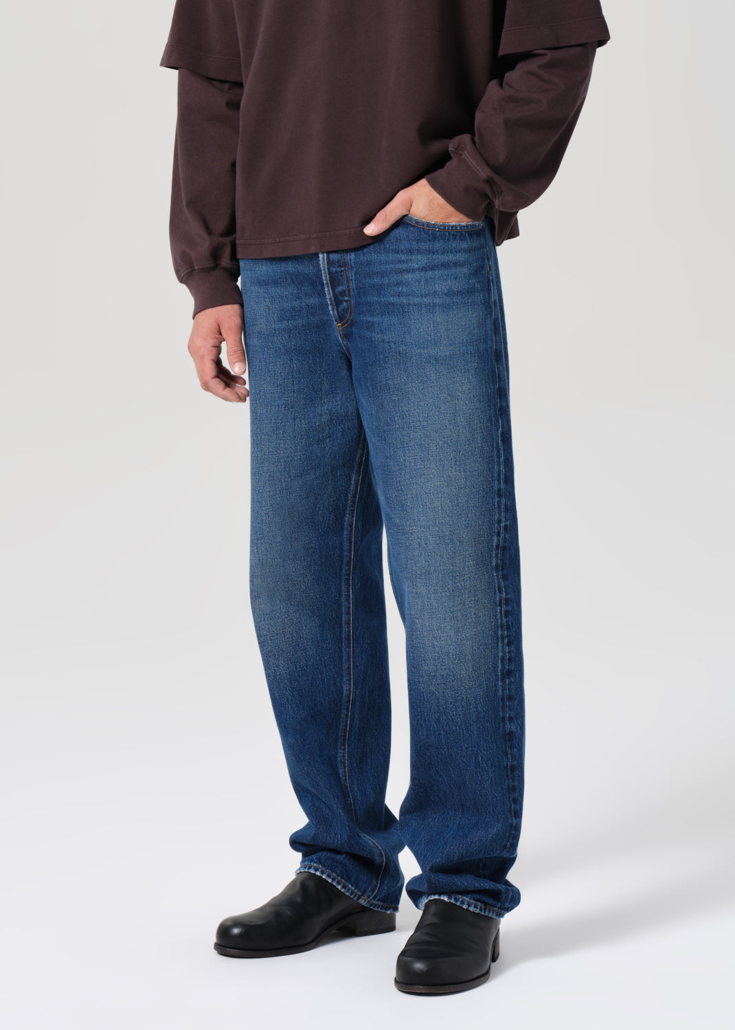 Person wearing blue jeans and a brown sweatshirt on a white background