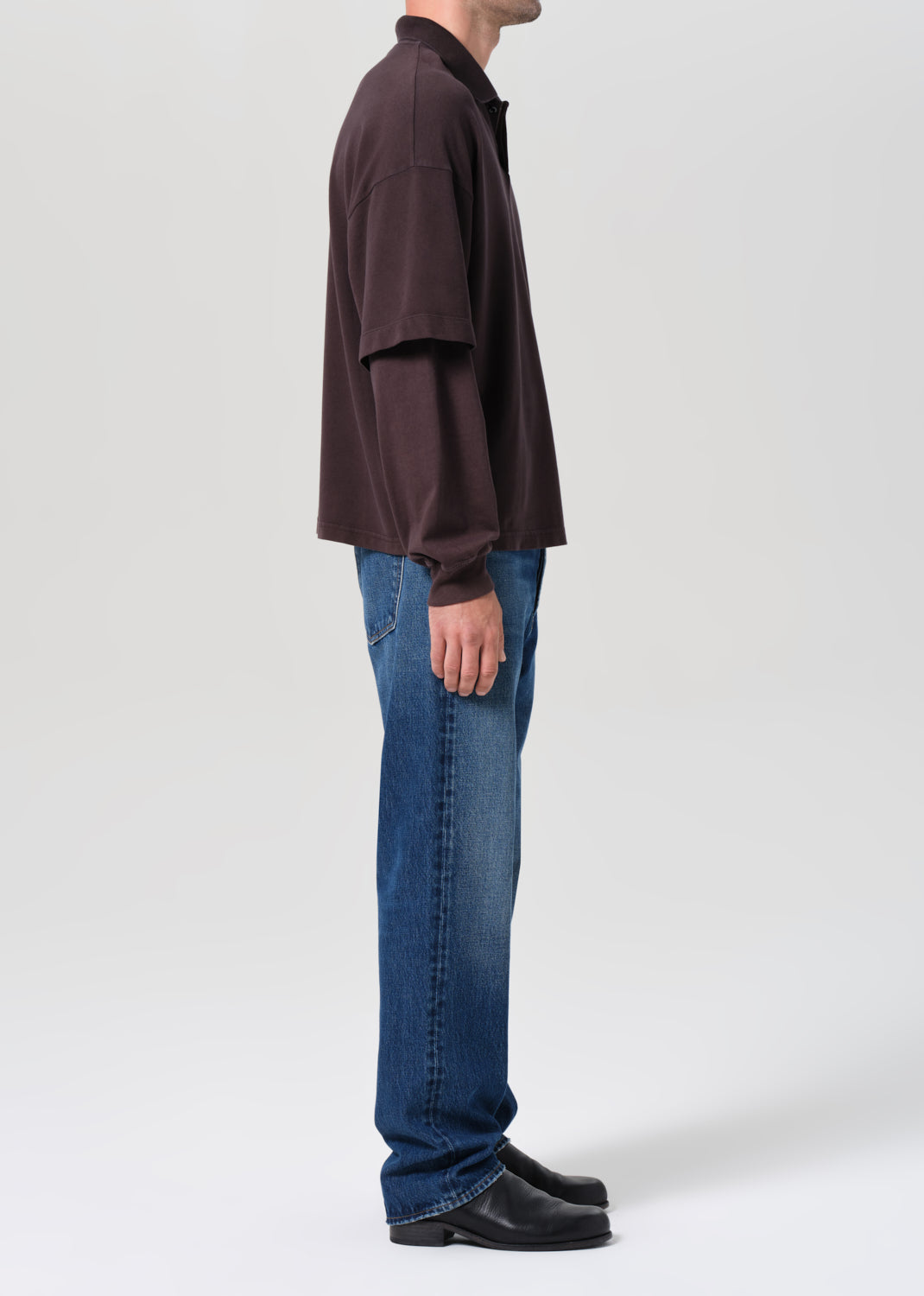 Person wearing a brown long-sleeve shirt and blue jeans on a white background