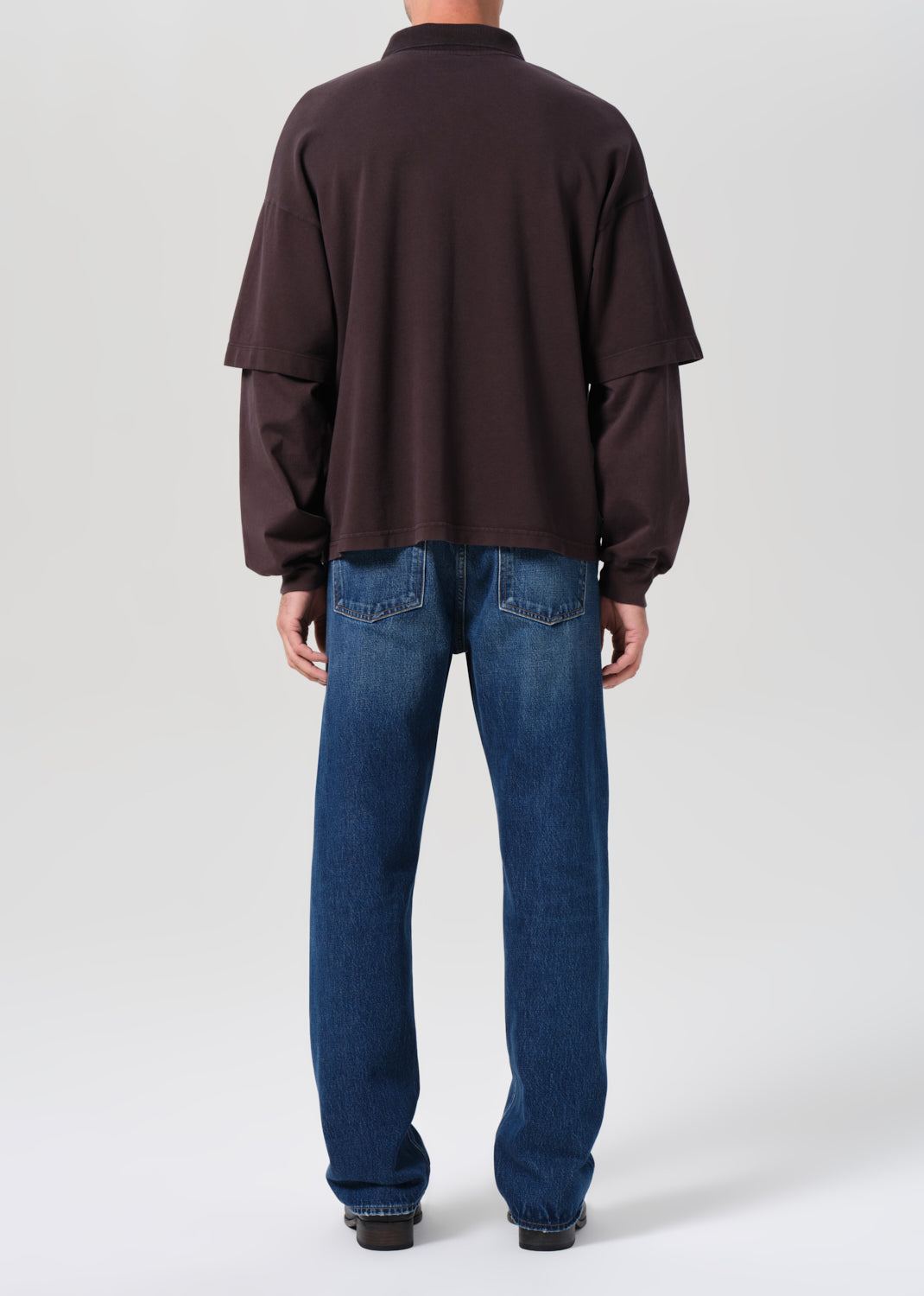 Person wearing a brown fleece jacket and blue jeans on a white background