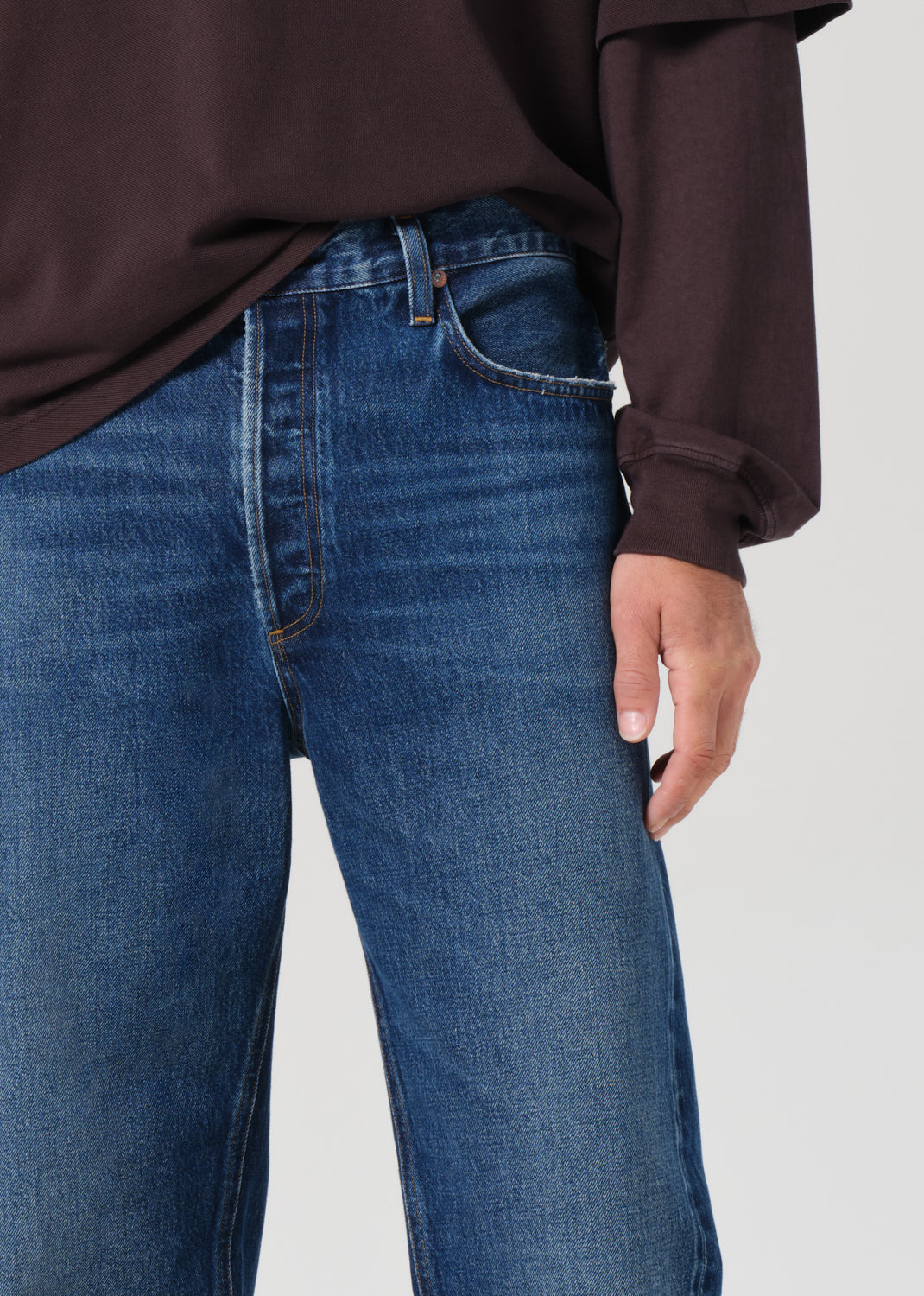 Person wearing blue jeans and a brown shirt on a plain background