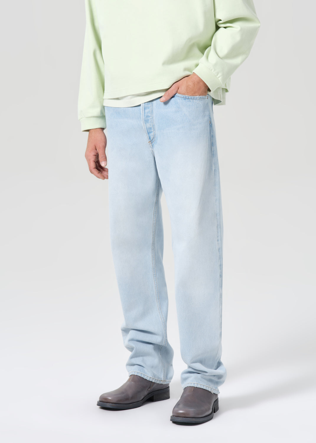 Person wearing light blue jeans and a light green sweater on a white background
