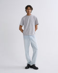 A man modeling a light gray crewneck t-shirt and light blue jeans with black shoes, standing against a plain light gray studio background.