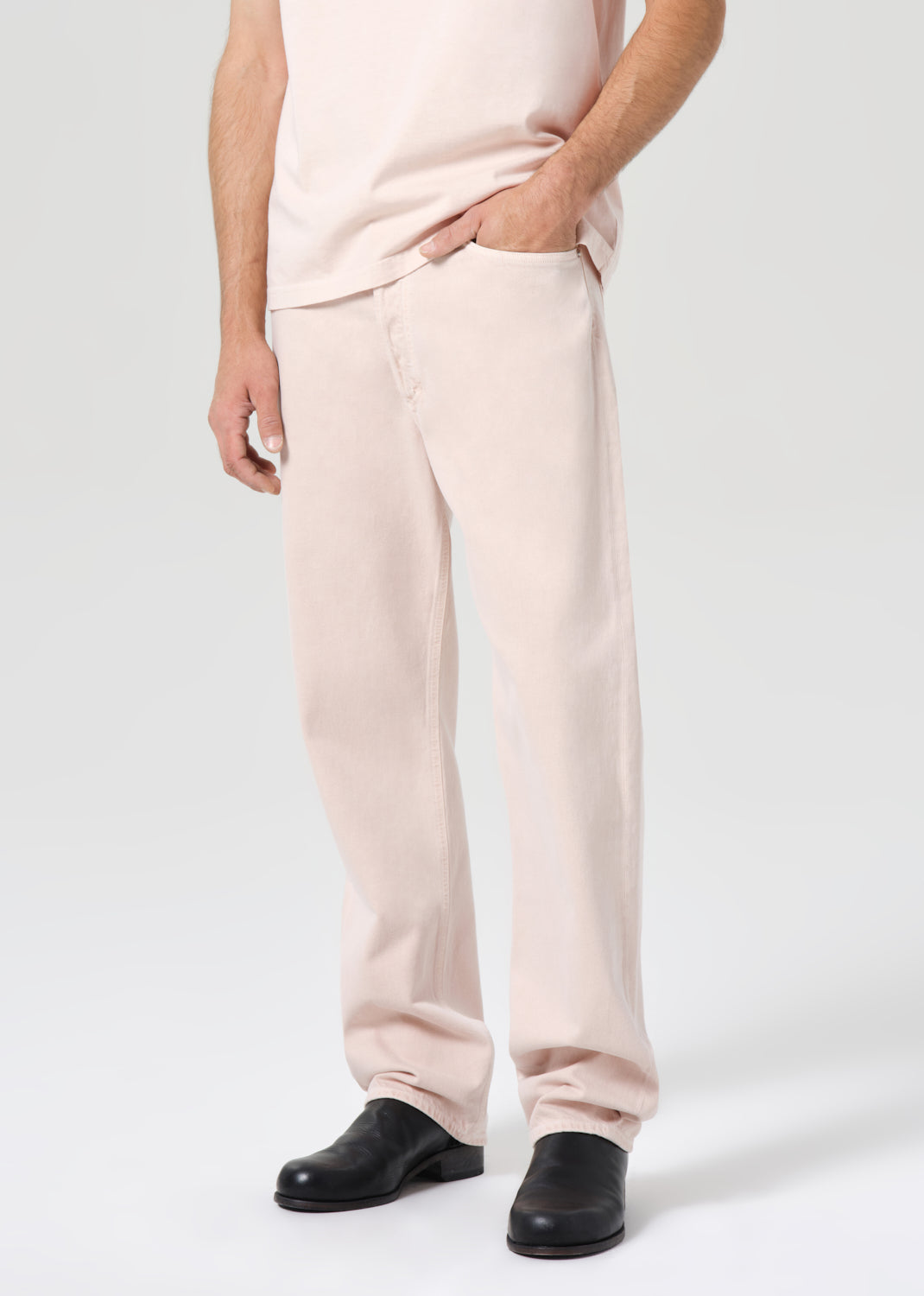Person wearing light pink pants and black shoes on a white background