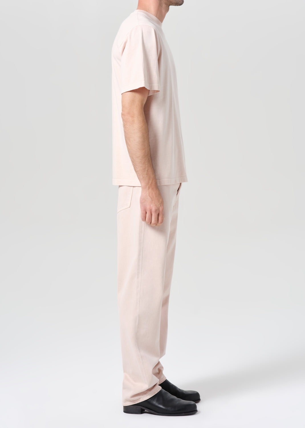 Person wearing a beige outfit with black shoes on a white background