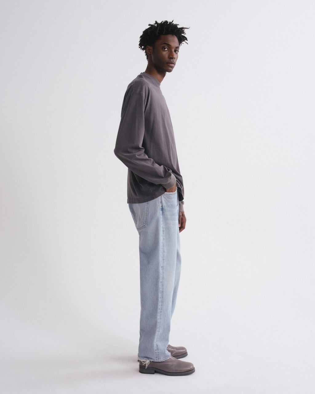 Man wearing a gray long-sleeve shirt and light blue jeans on a white background