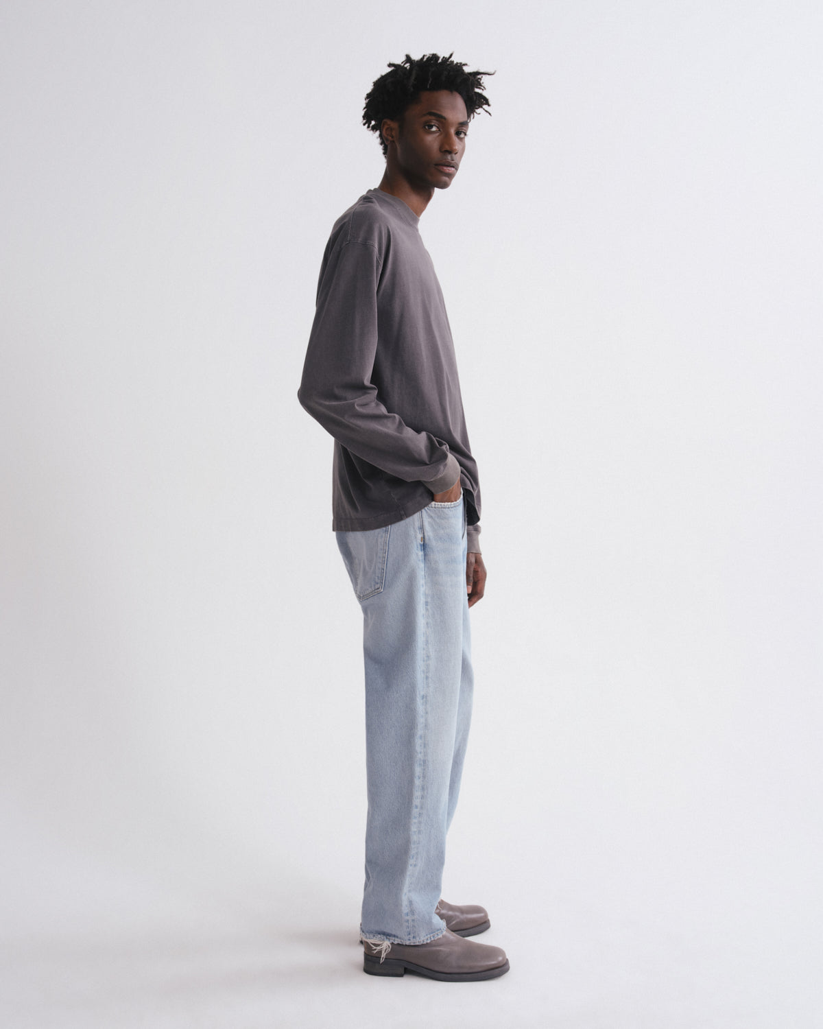 Man wearing a gray long-sleeve shirt and light blue jeans on a white background