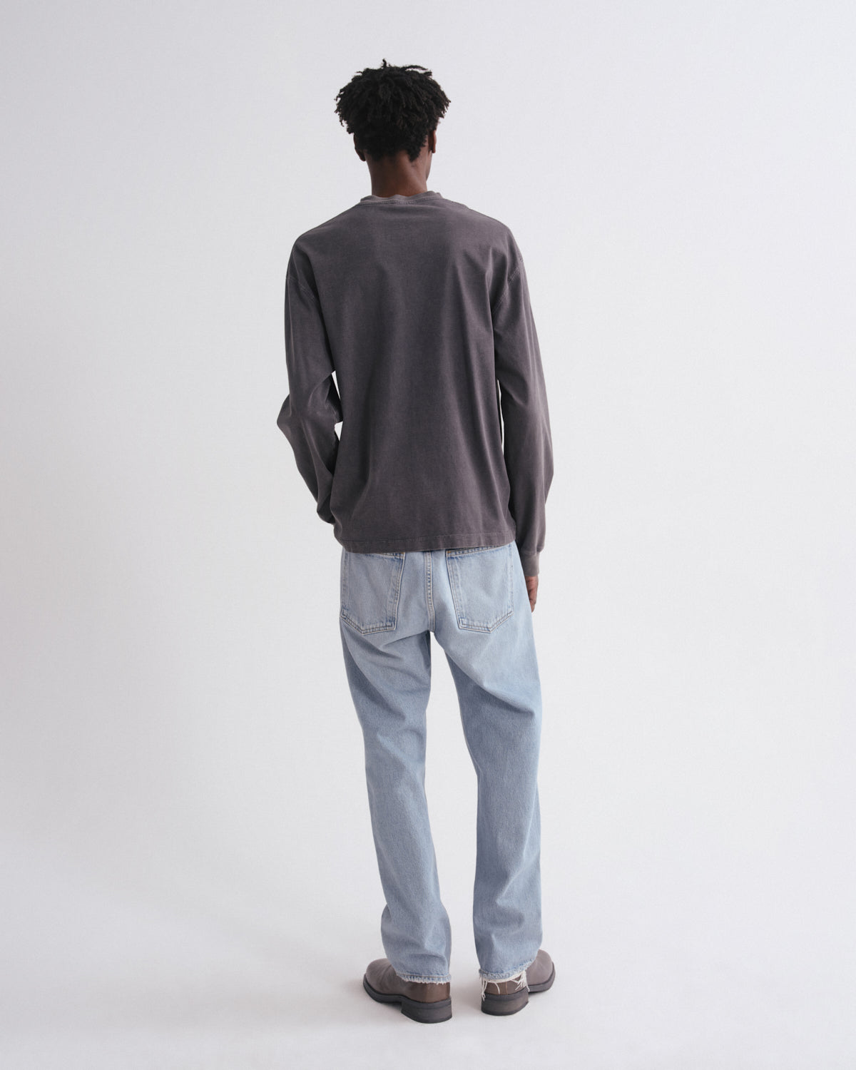 Person wearing a dark gray long-sleeve shirt and light blue jeans on a white background