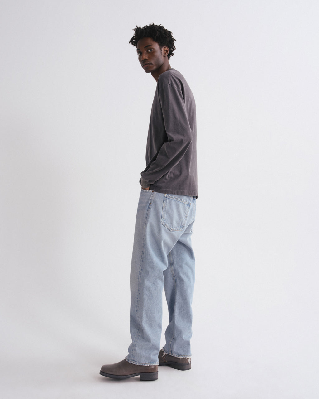 Man wearing a gray long-sleeve shirt and light blue jeans on a white background
