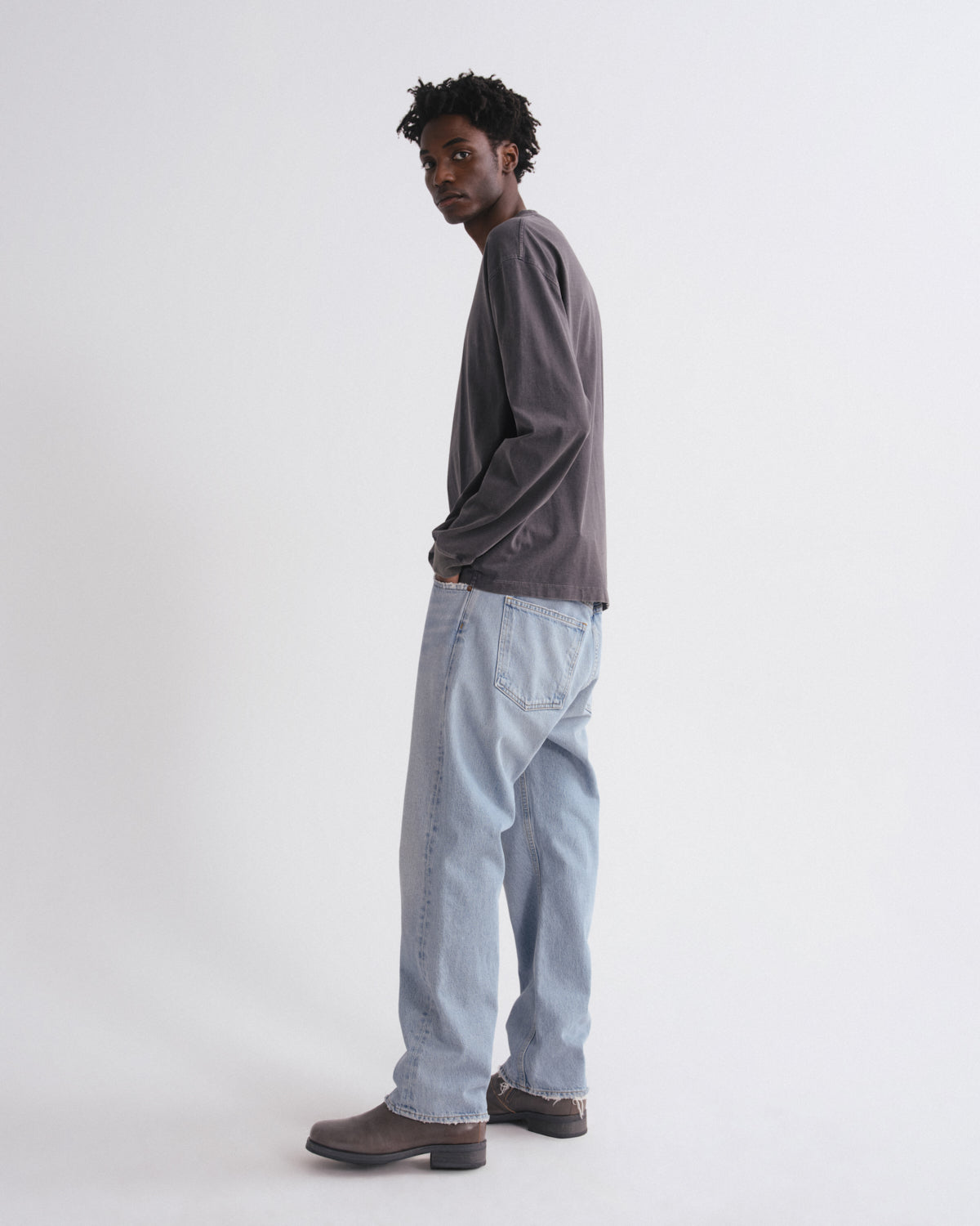 Man wearing a gray long-sleeve shirt and light blue jeans on a white background