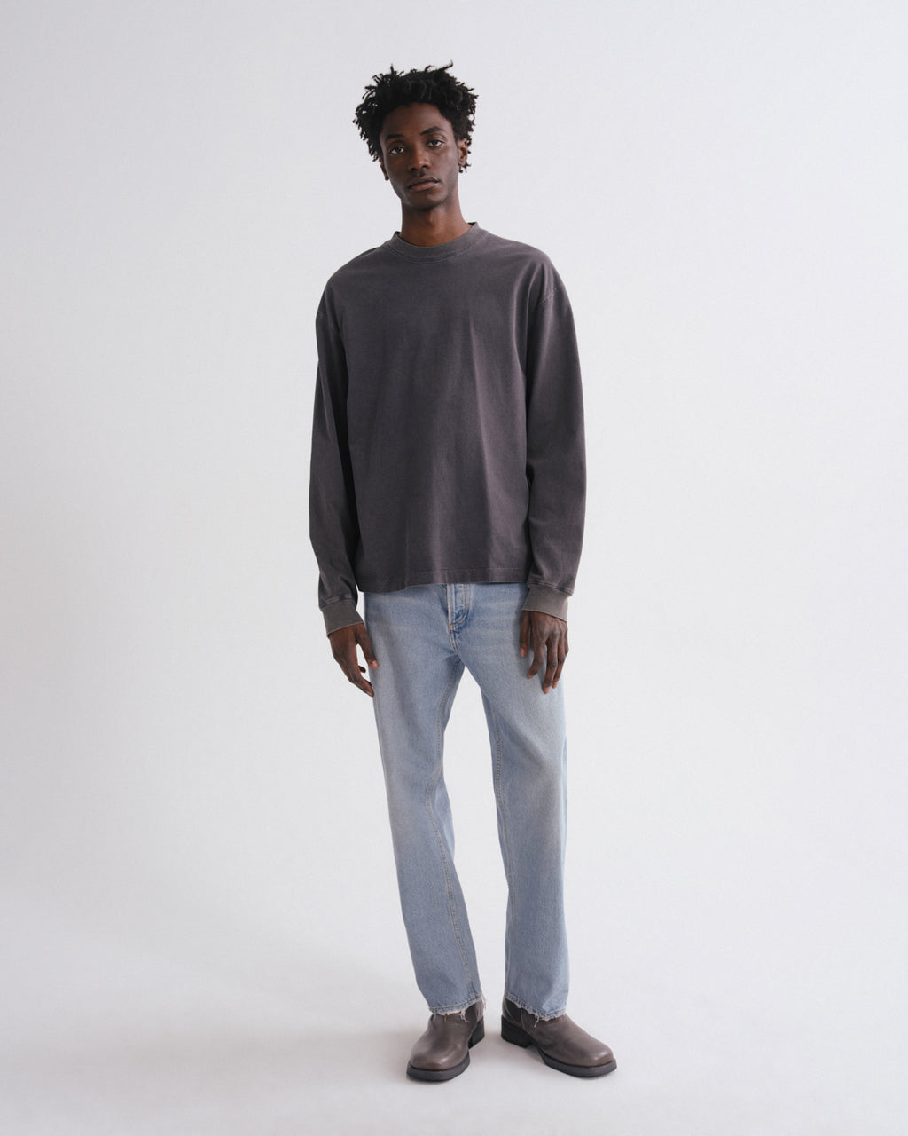 Man wearing a dark gray sweater and light blue jeans on a white background