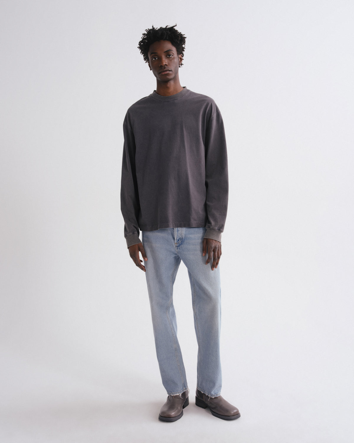 Man wearing a dark gray sweater and light blue jeans on a white background