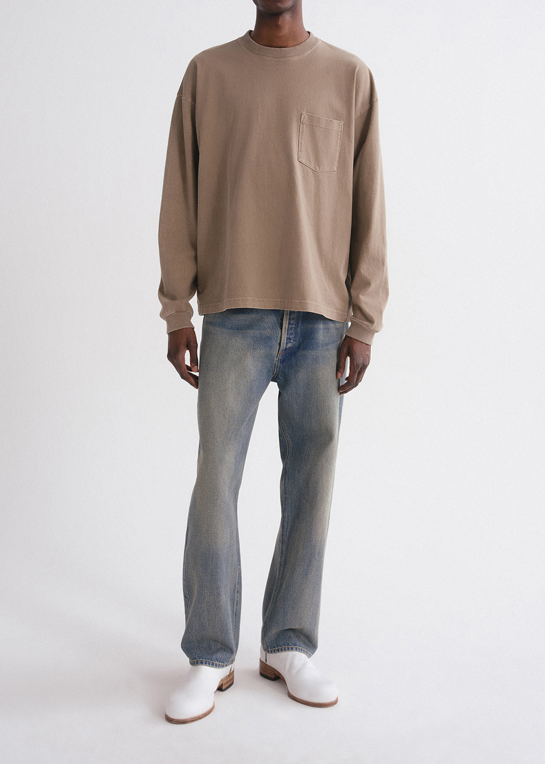 Person wearing a beige long-sleeve shirt and blue jeans on a grey background