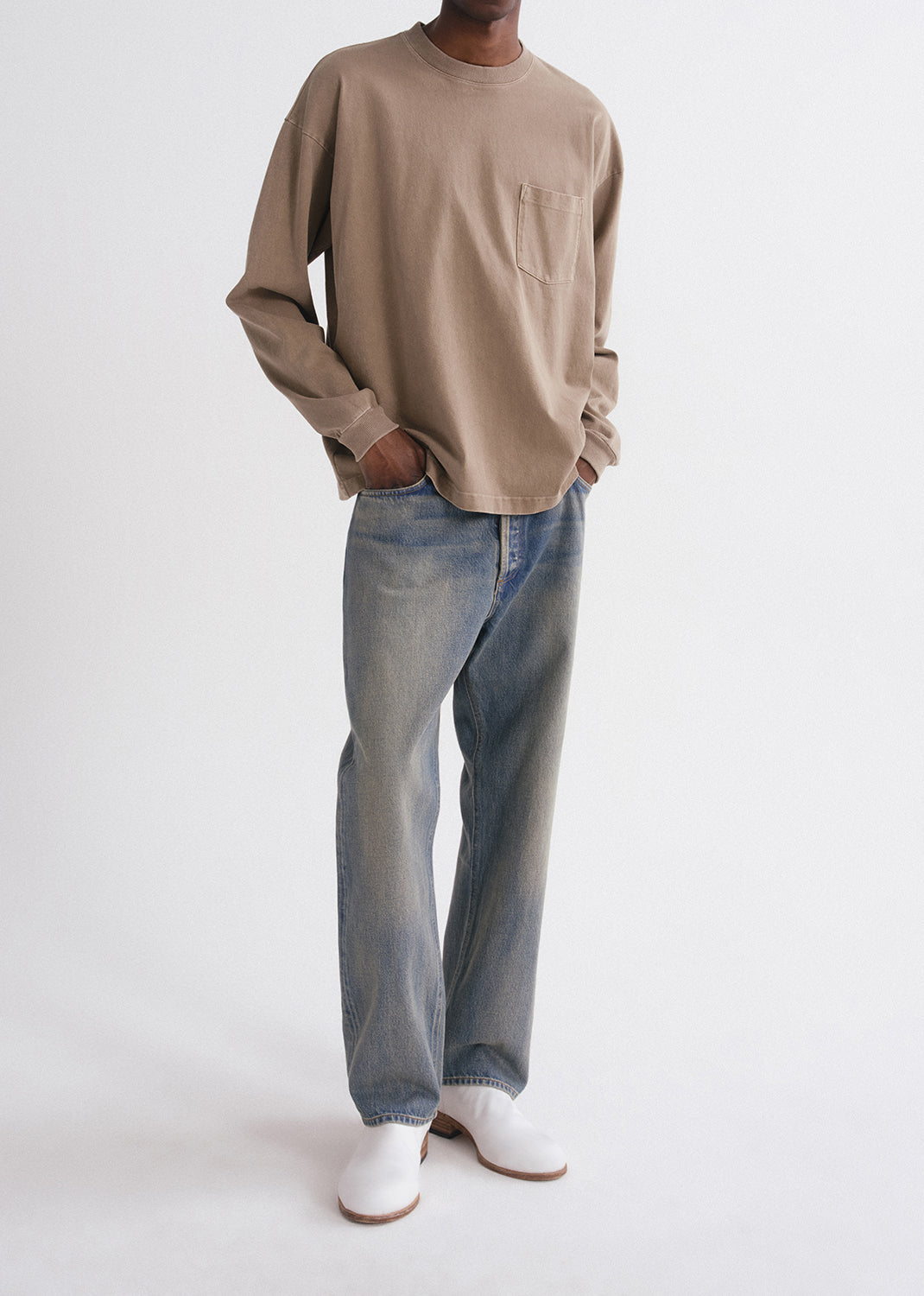 Person wearing a beige long-sleeve shirt and blue jeans on a grey background