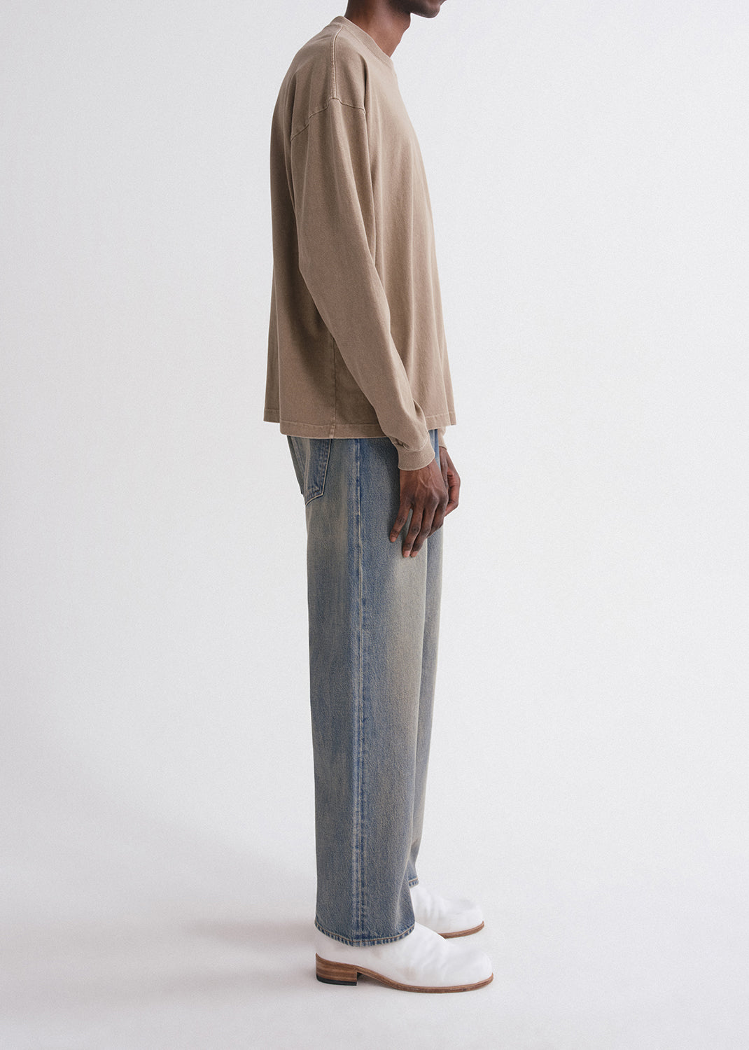 Person wearing a beige sweater and blue jeans on a grey background