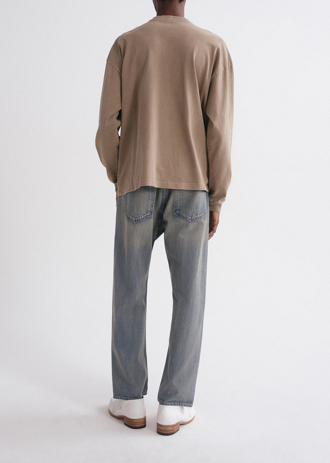 Person wearing a beige long-sleeve shirt and light blue jeans on a grey background