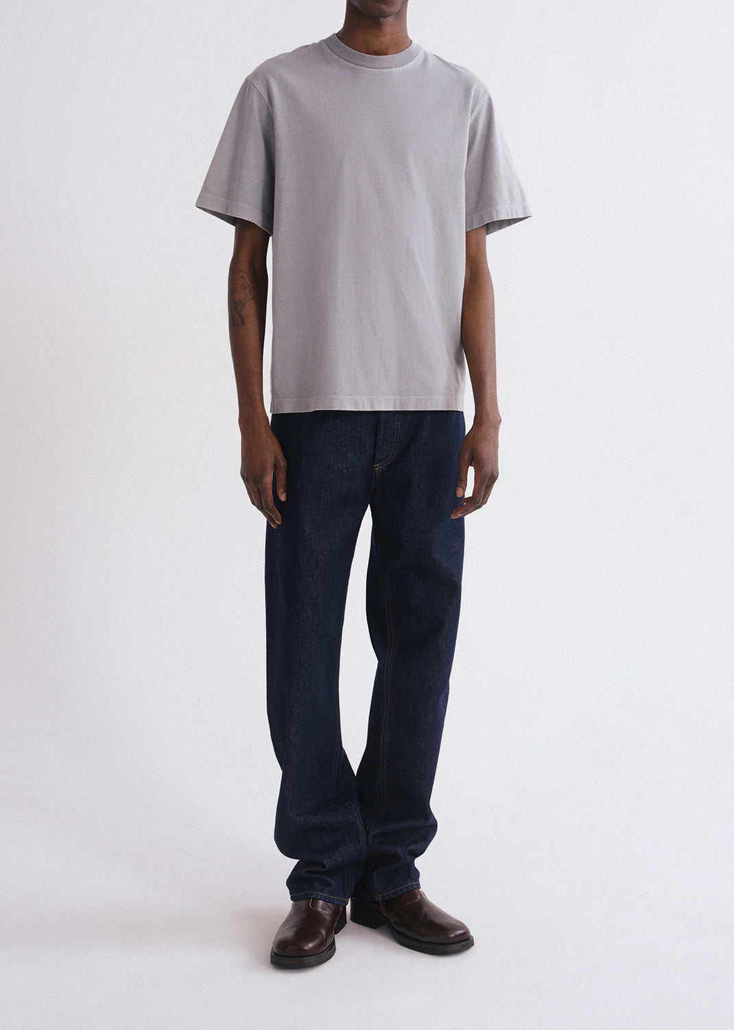 Person wearing a grey t-shirt and dark jeans on a grey background
