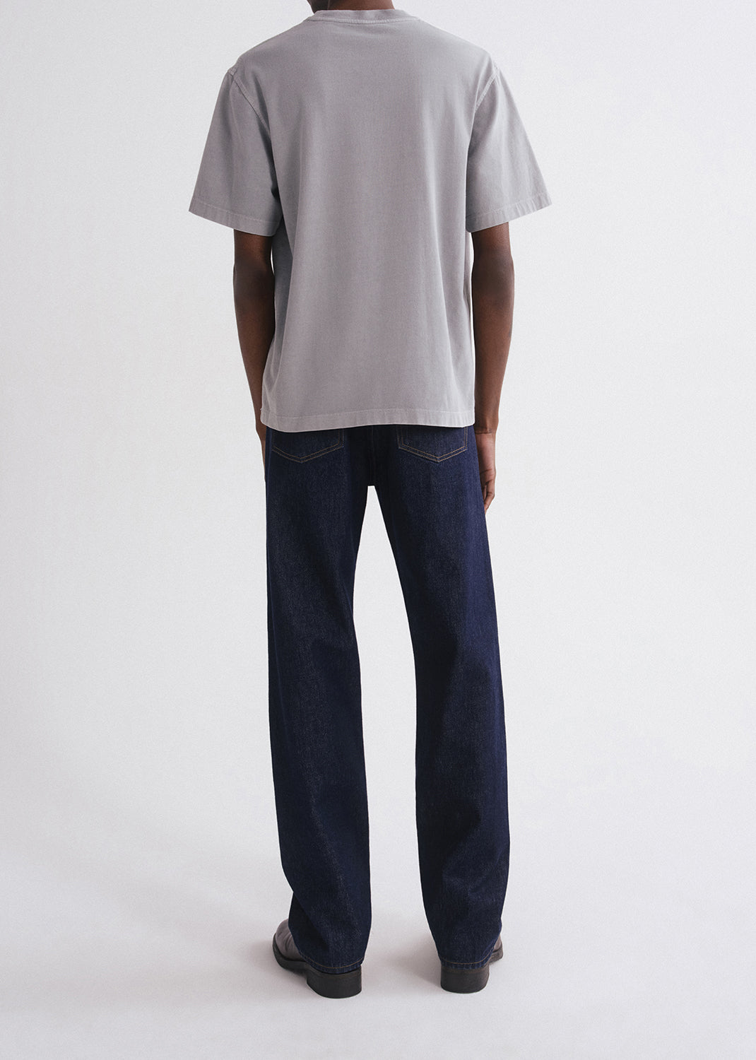 Person wearing a grey t-shirt and dark jeans on a grey background