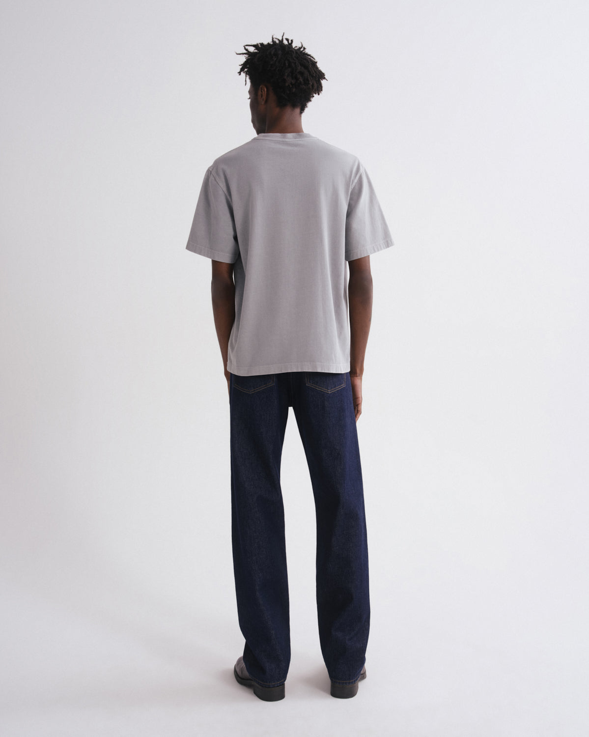 Person wearing a plain gray t-shirt and dark jeans on a white background
