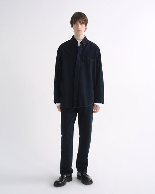 Person wearing a black long sleeve shirt with black pants and black shoes on a grey background