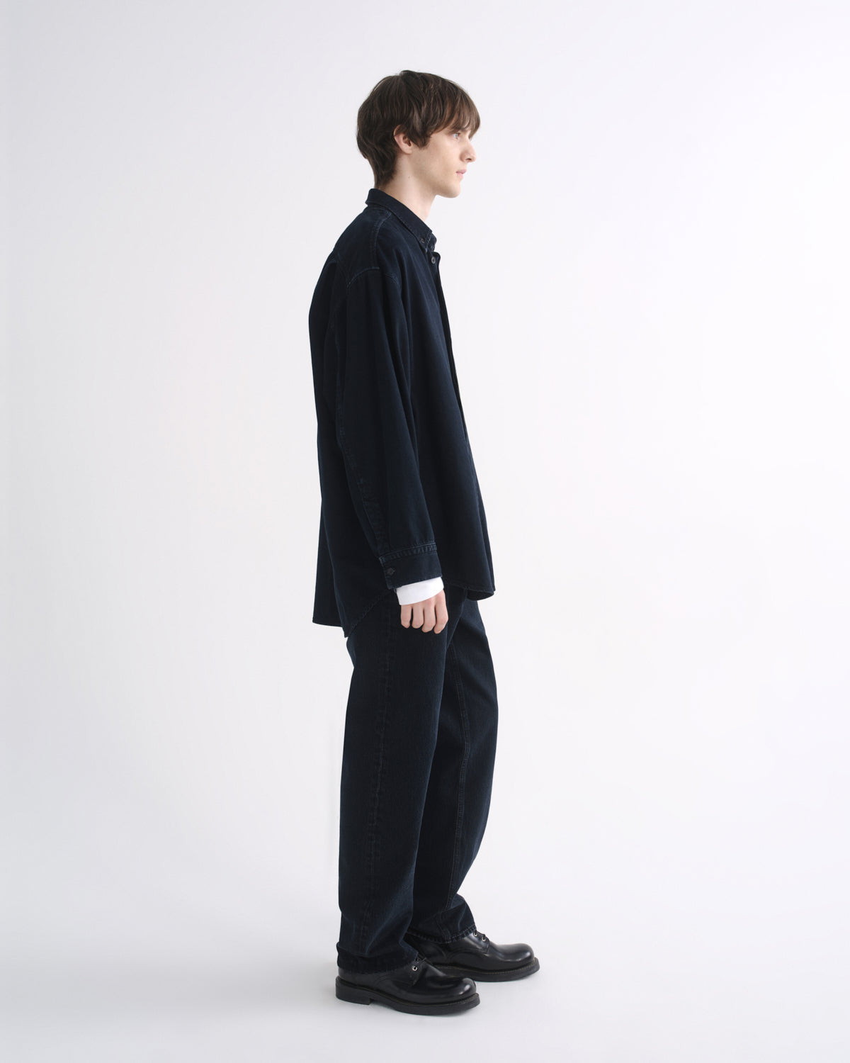 Person wearing a black long sleeve shirt with black pants and black shoes, side view, on a grey background