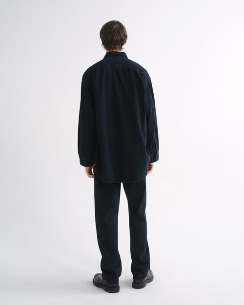 Person wearing a black long sleeve shirt with black pants and black shoes, back view, on a grey background