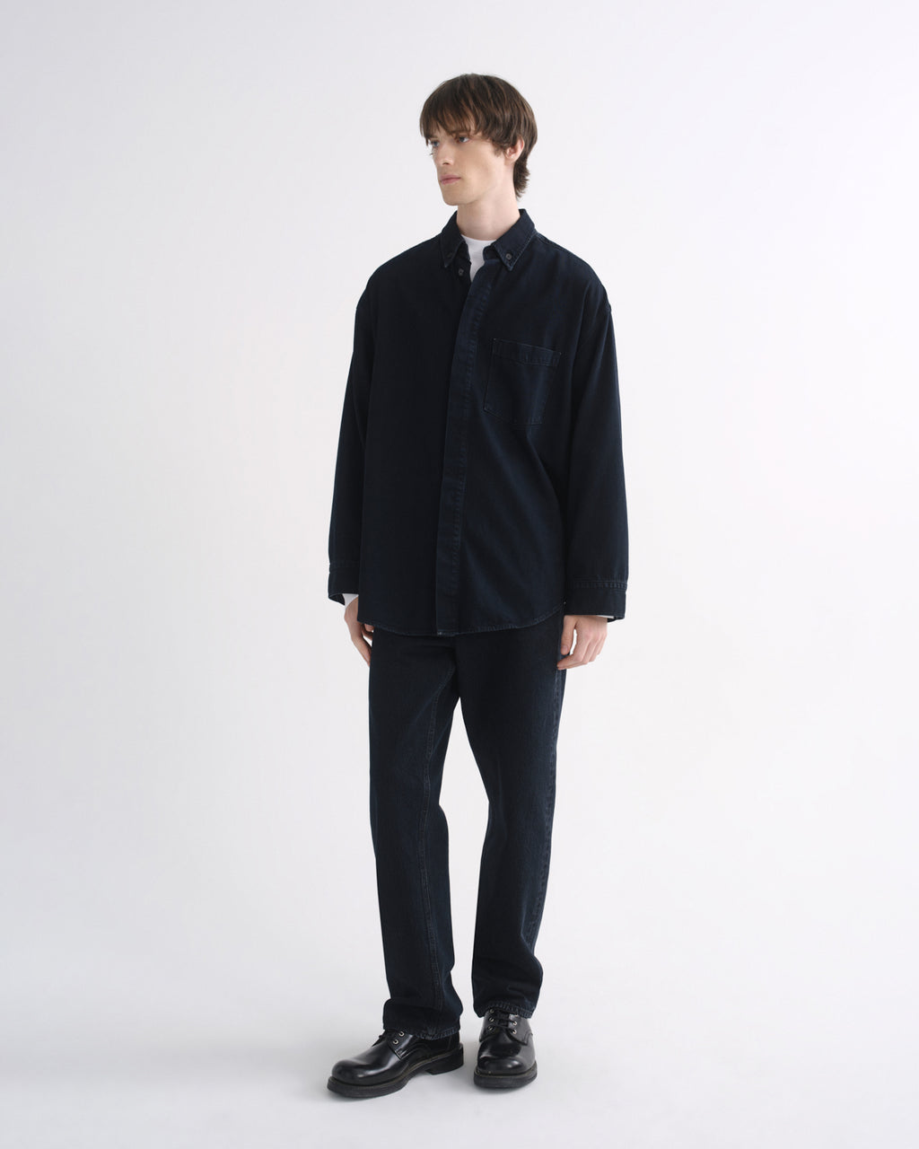 Person wearing a black long sleeve shirt with black pants and black shoes on a grey background
