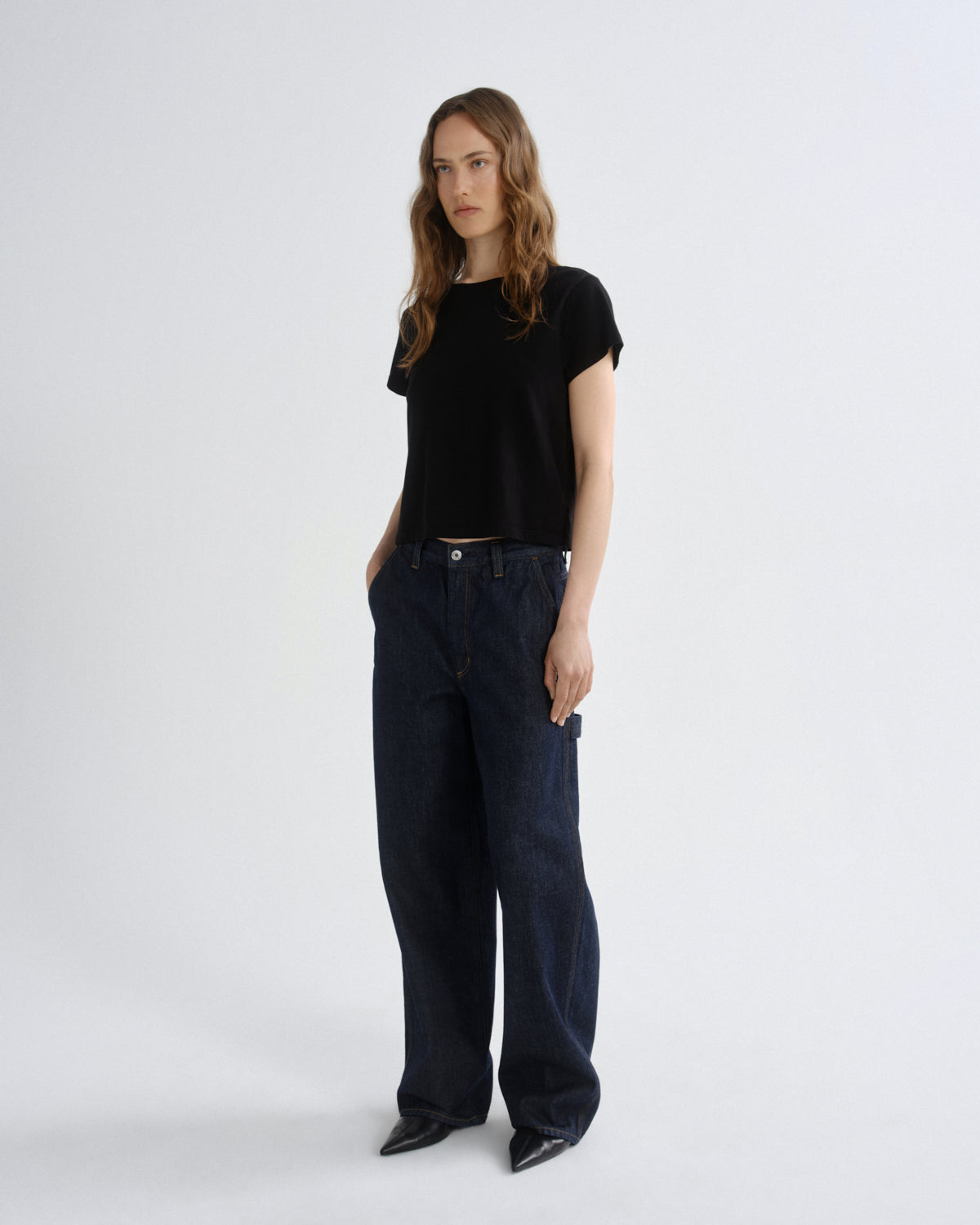 Woman wearing a black t-shirt and dark jeans on a white background