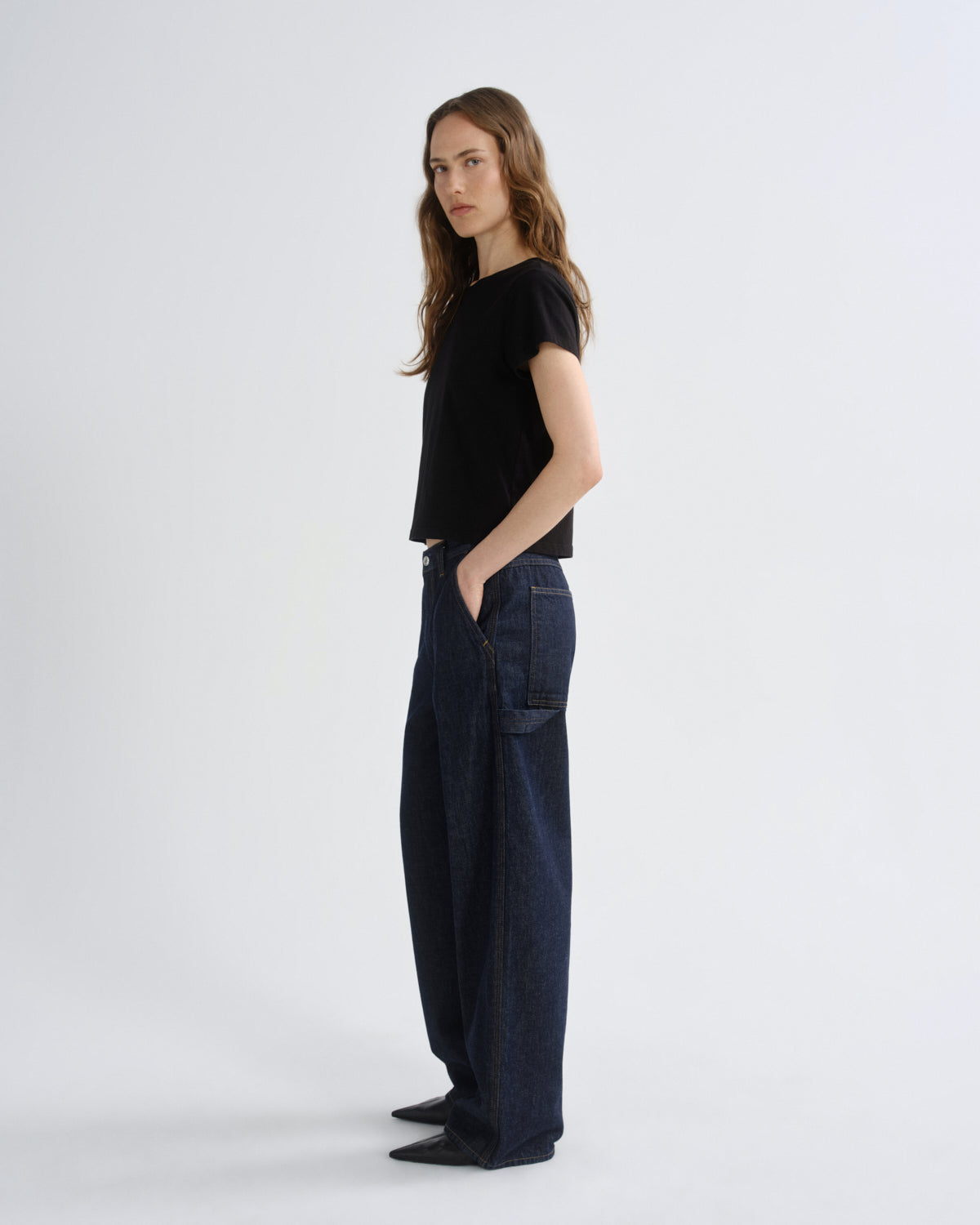 Woman wearing a black top and dark jeans on a white background