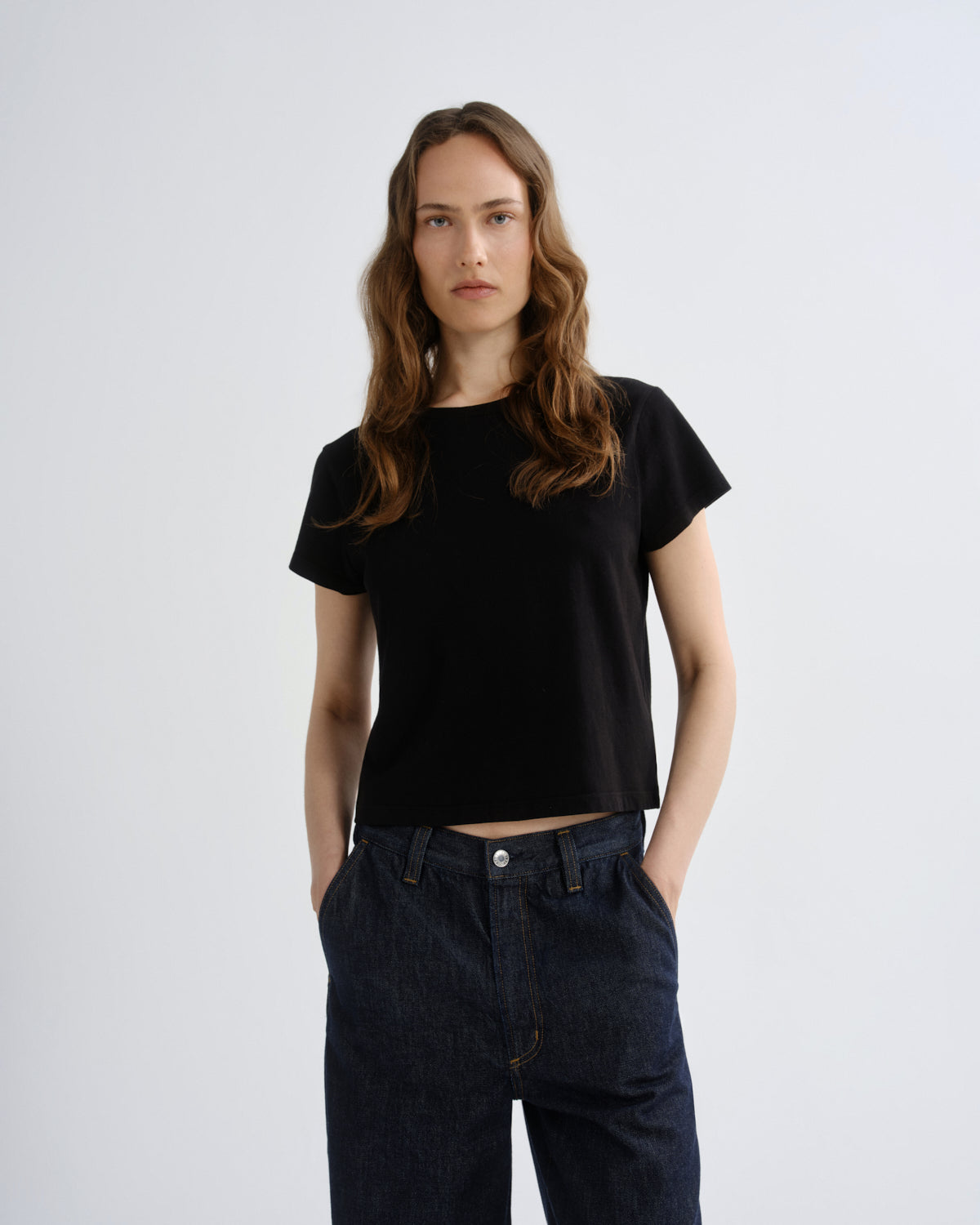 Person wearing a black t-shirt and dark jeans on a white background