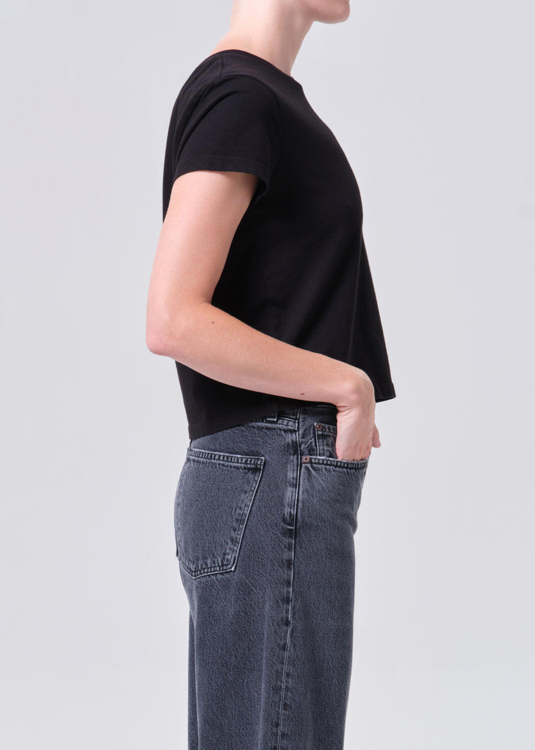 Person wearing a black t-shirt and blue jeans on a light gray background