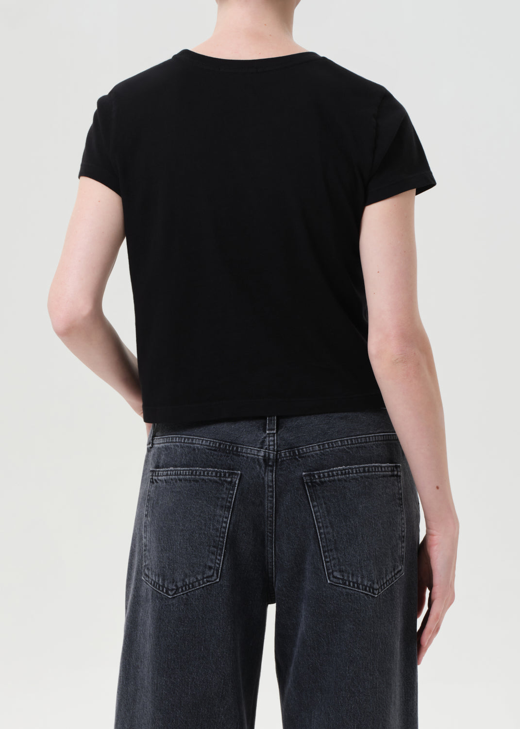 Person wearing a black t-shirt and dark jeans on a plain background