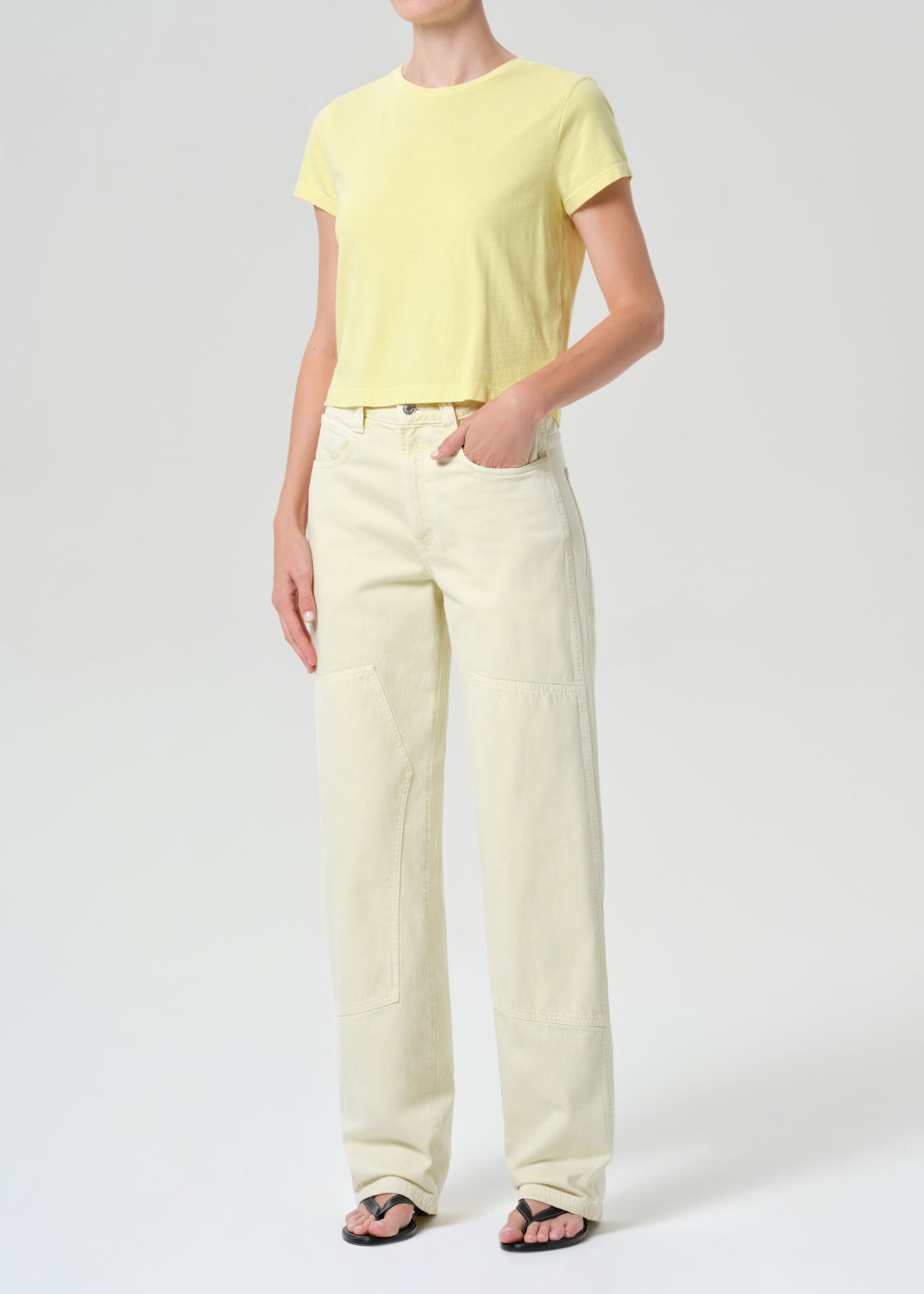 Person wearing a yellow t-shirt and light-colored pants on a white background
