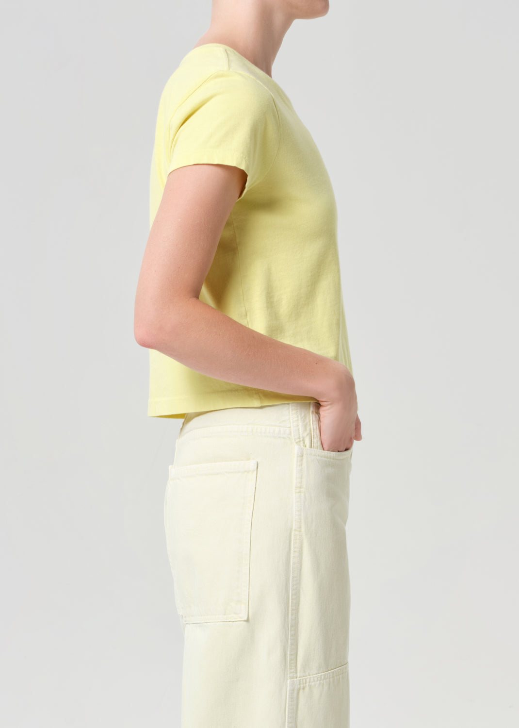 Person wearing a light yellow t-shirt and white pants on a plain background