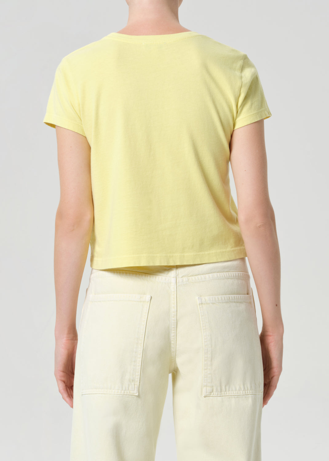 Person wearing a yellow t-shirt and light-colored pants on a plain background